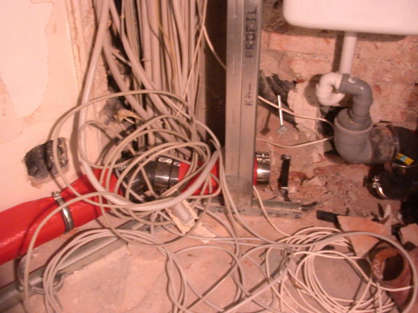 Elektro- und Sanitärinstallation im Rohbau: Kabelbündel, rote Brandschutz-/Leitung und Siphon an geöffneter WandMünchen