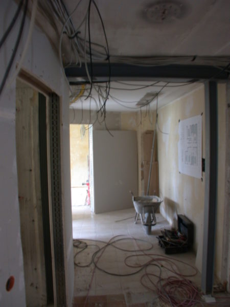 Rohbauflur mit frei hängenden Leitungen, Stahlträger, Werkzeugkiste und Schubkarre – Elektroinstallation Praxis Dr. Naumann