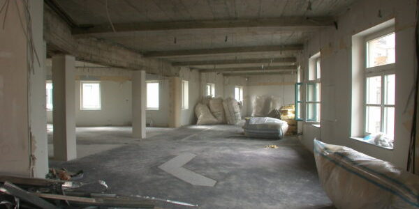 Elektro- und Sanitärinstallation im Rohbau: Kabelbündel, rote Brandschutz-/Leitung und Siphon an geöffneter Wand