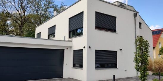 Außenansicht eines modernen Einfamilienhauses in Dachau mit grauer Putzfassade, Fenstern mit Rollläden