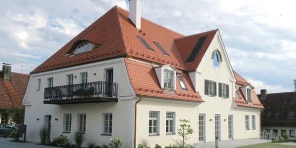 Außenansicht eines modernen Mehrfamilienhauses mit rotem Satteldach, Balkonen und saniertem Fassadenkonzept.